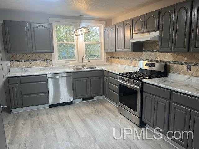 kitchen with gray cabinetry, light stone countertops, sink, light hardwood / wood-style floors, and appliances with stainless steel finishes