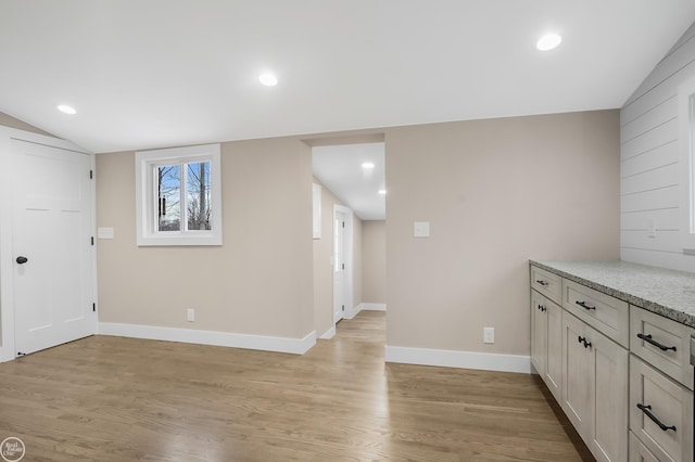 interior space featuring light stone counters, light hardwood / wood-style flooring, and vaulted ceiling