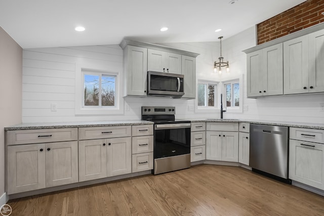 kitchen with vaulted ceiling, decorative light fixtures, sink, light hardwood / wood-style floors, and stainless steel appliances