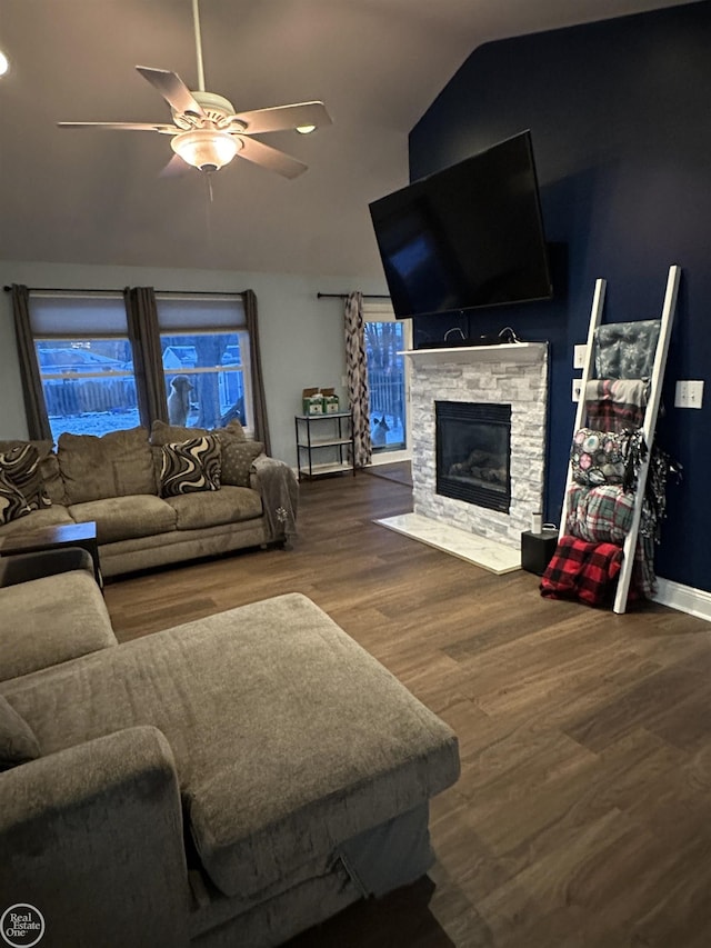 living room featuring hardwood / wood-style flooring, ceiling fan, a stone fireplace, and vaulted ceiling