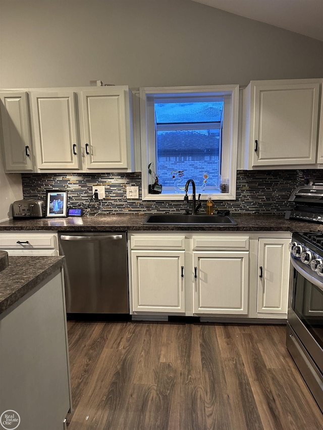 kitchen featuring appliances with stainless steel finishes, dark hardwood / wood-style flooring, vaulted ceiling, sink, and white cabinetry