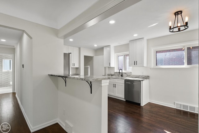 kitchen with kitchen peninsula, appliances with stainless steel finishes, a breakfast bar, decorative light fixtures, and white cabinetry