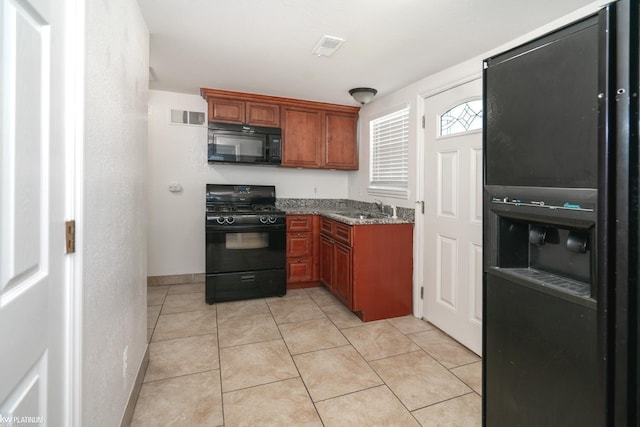 kitchen with black appliances, light tile patterned floors, sink, and stone counters