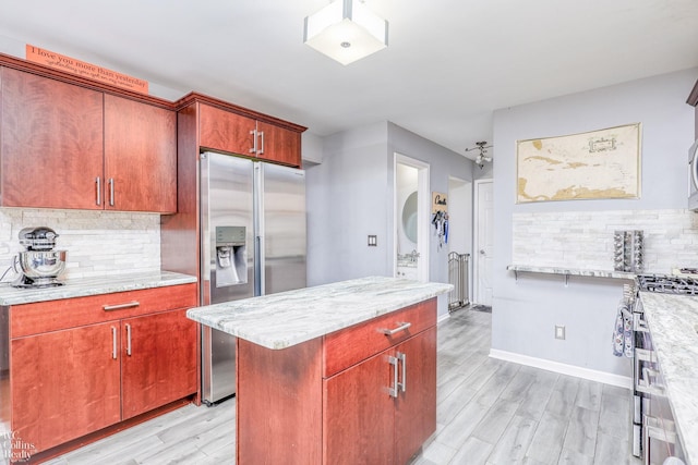 kitchen with backsplash, light stone counters, light wood-type flooring, and appliances with stainless steel finishes