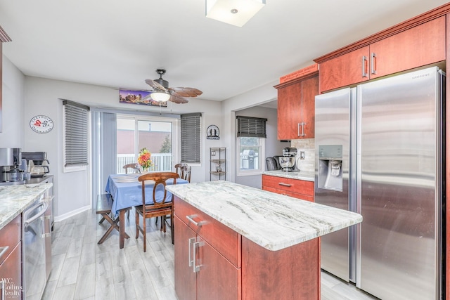 kitchen with ceiling fan, light stone countertops, light wood-type flooring, appliances with stainless steel finishes, and a kitchen island