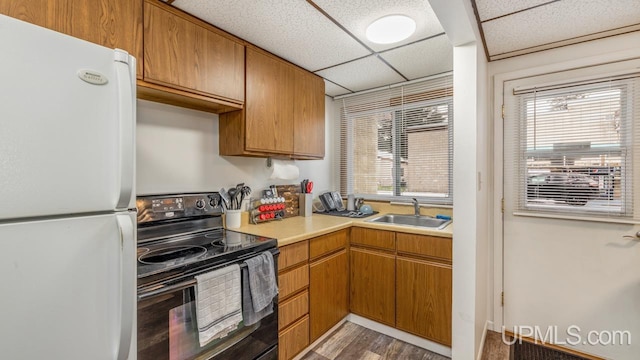 kitchen featuring light wood-type flooring, a drop ceiling, sink, white refrigerator, and black electric range