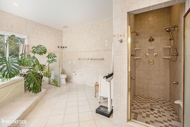 bathroom featuring tile patterned flooring, a shower with door, toilet, and tile walls