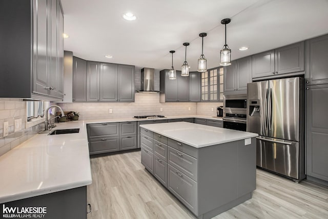 kitchen featuring sink, wall chimney exhaust hood, gray cabinets, a kitchen island, and appliances with stainless steel finishes