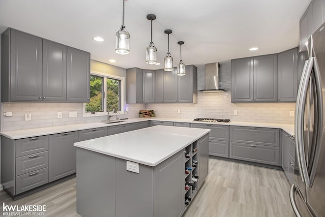 kitchen featuring gray cabinetry, sink, wall chimney range hood, decorative light fixtures, and a kitchen island