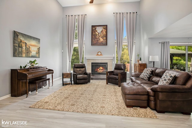 living room featuring a tiled fireplace, light hardwood / wood-style flooring, and a high ceiling