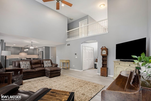 living room with light hardwood / wood-style flooring, a towering ceiling, and ceiling fan with notable chandelier