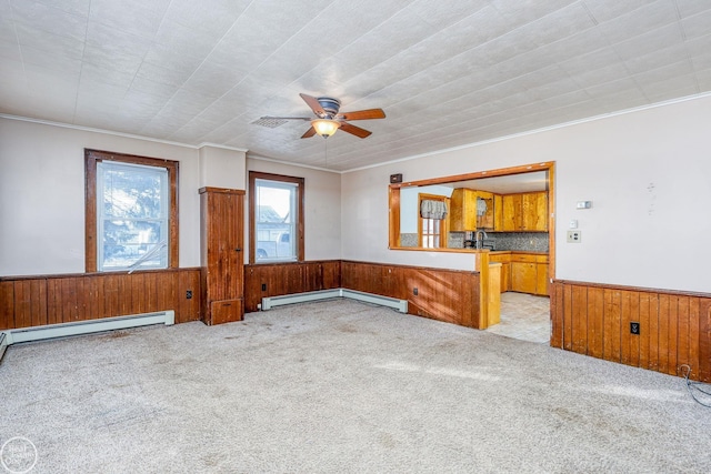 unfurnished living room with ceiling fan, wood walls, light colored carpet, and baseboard heating