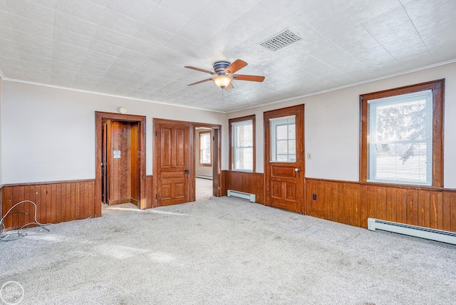 carpeted empty room with a wealth of natural light, wooden walls, and a baseboard radiator