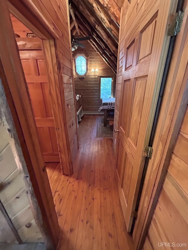 corridor with wood walls, wood-type flooring, and lofted ceiling