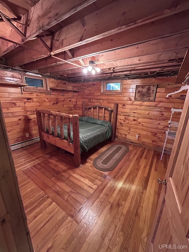 unfurnished bedroom with baseboard heating, wooden walls, and wood-type flooring