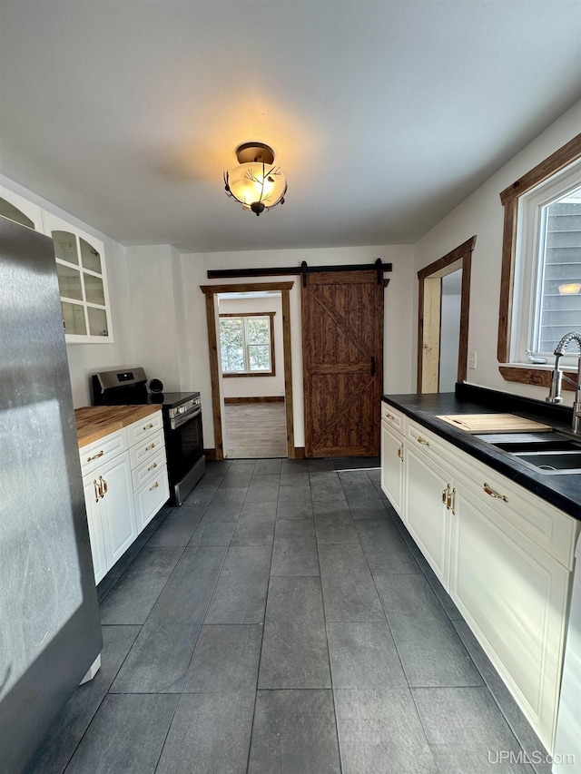 kitchen featuring white cabinets, sink, stainless steel range with electric stovetop, fridge, and a barn door