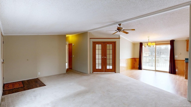 carpeted spare room with french doors, ornamental molding, ceiling fan with notable chandelier, a textured ceiling, and wooden walls