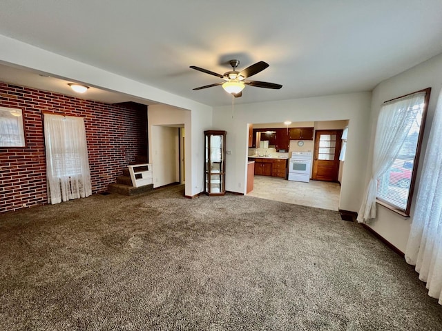 unfurnished living room featuring ceiling fan, light colored carpet, and brick wall