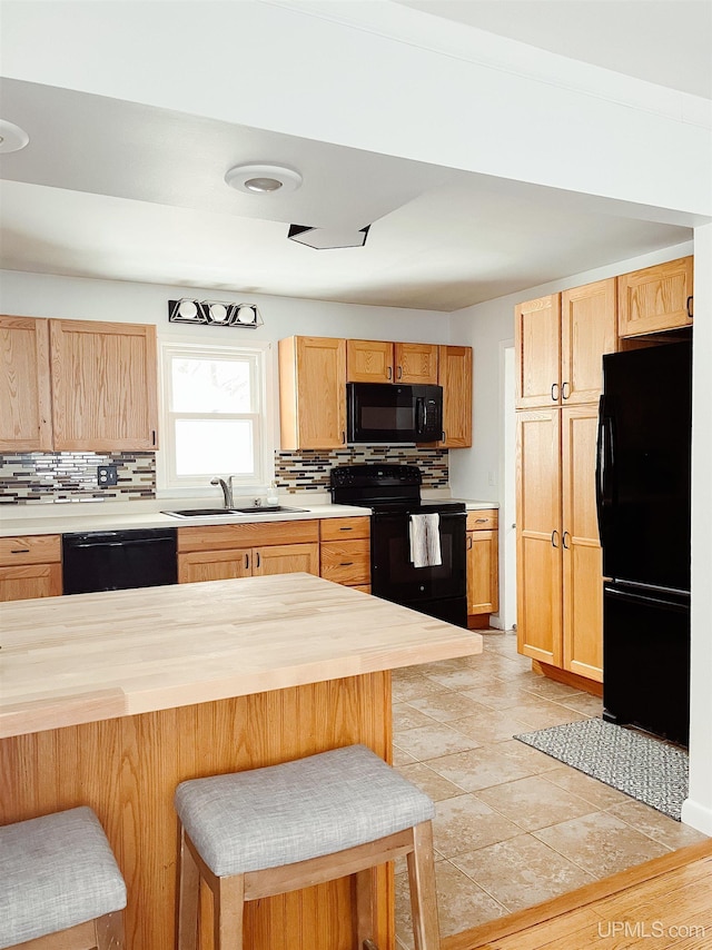 kitchen with black appliances, sink, decorative backsplash, butcher block countertops, and a breakfast bar area