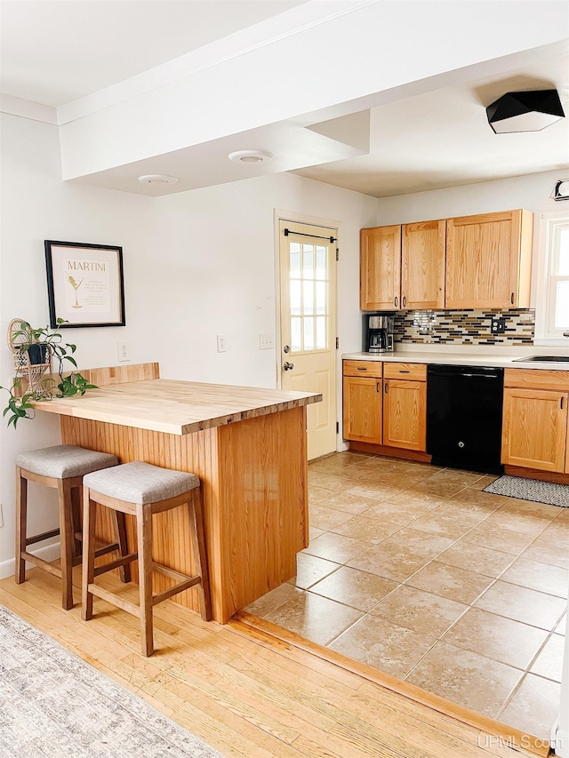 kitchen with a kitchen breakfast bar, sink, light wood-type flooring, black dishwasher, and tasteful backsplash