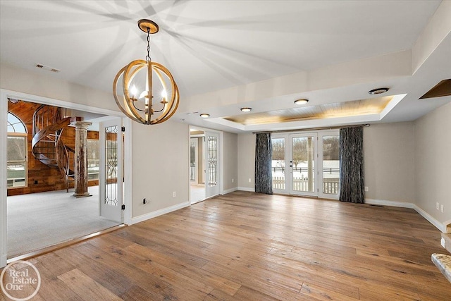 empty room featuring a raised ceiling, french doors, light wood-type flooring, and an inviting chandelier