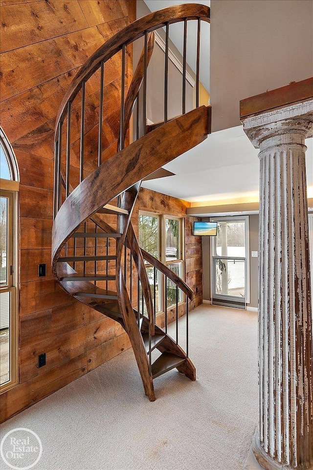 stairway featuring carpet flooring, wooden walls, decorative columns, and a healthy amount of sunlight