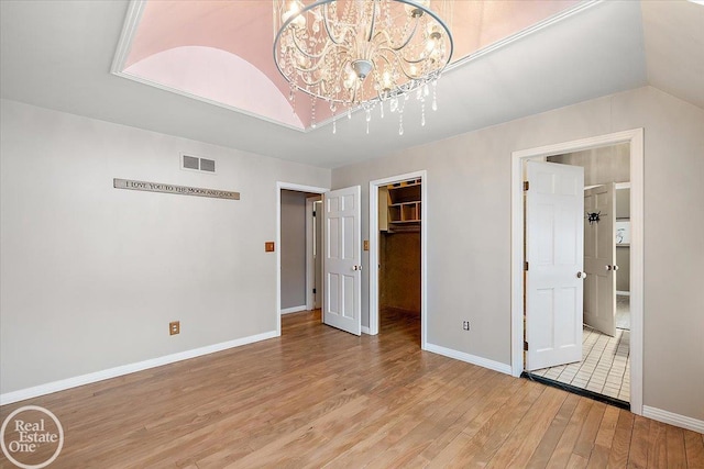 unfurnished bedroom with a closet, light wood-type flooring, a spacious closet, and a chandelier