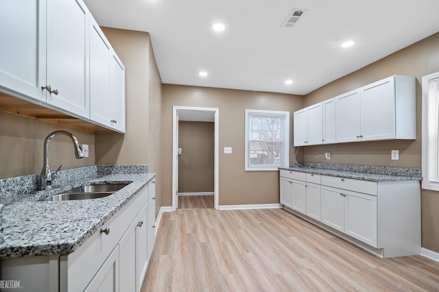 kitchen with white cabinetry, sink, light stone countertops, and light wood-type flooring