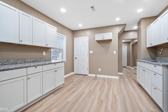 kitchen featuring light stone countertops, white cabinetry, and sink