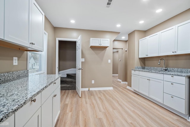 kitchen featuring light stone countertops, light hardwood / wood-style floors, white cabinetry, and sink