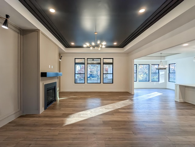 unfurnished living room featuring a chandelier, hardwood / wood-style floors, a tray ceiling, and ornamental molding