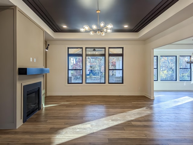 unfurnished living room featuring ceiling fan with notable chandelier, dark hardwood / wood-style flooring, a raised ceiling, and ornamental molding