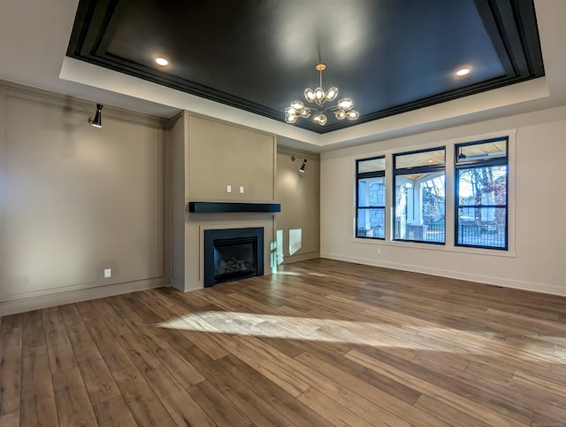 unfurnished living room featuring a chandelier, hardwood / wood-style floors, a raised ceiling, and ornamental molding