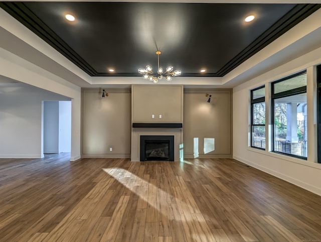 unfurnished living room with a tray ceiling, hardwood / wood-style flooring, crown molding, and an inviting chandelier