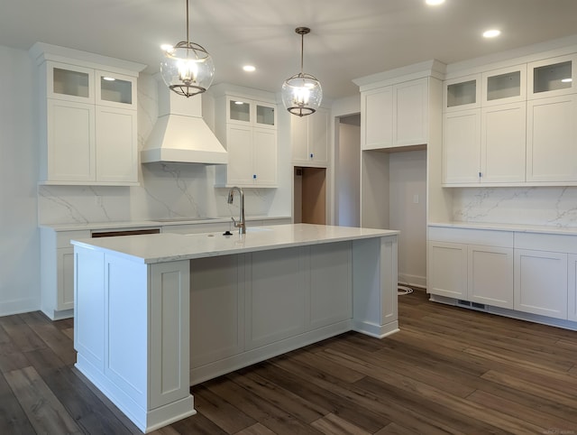 kitchen with premium range hood, a kitchen island with sink, dark wood-type flooring, pendant lighting, and white cabinetry