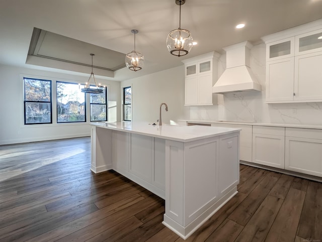 kitchen with white cabinets, a raised ceiling, custom range hood, and a kitchen island with sink