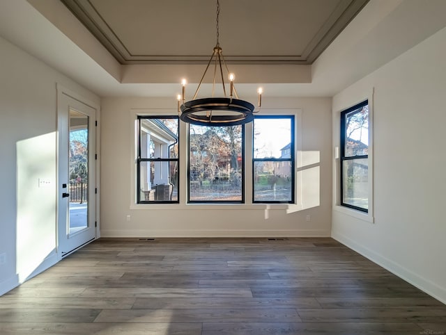 unfurnished dining area with an inviting chandelier, dark hardwood / wood-style flooring, ornamental molding, and a tray ceiling