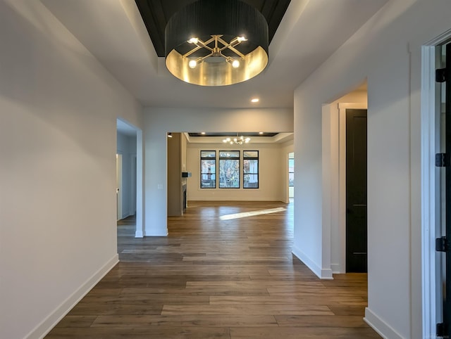 corridor with hardwood / wood-style flooring, an inviting chandelier, and a tray ceiling