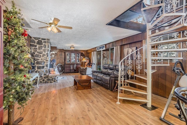 living room with a textured ceiling, light hardwood / wood-style flooring, ceiling fan, and wooden walls