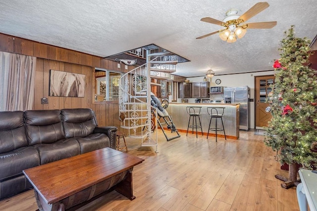 living room with wooden walls, ceiling fan, light hardwood / wood-style floors, and a textured ceiling