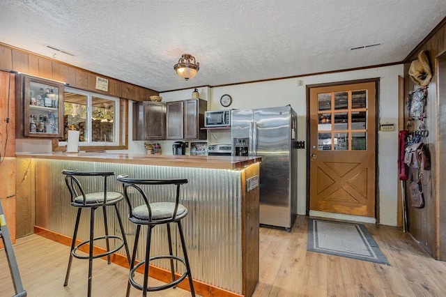 kitchen with wood walls, a kitchen breakfast bar, crown molding, built in microwave, and kitchen peninsula