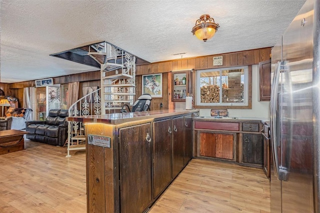 kitchen with wood walls, kitchen peninsula, a textured ceiling, and stainless steel refrigerator