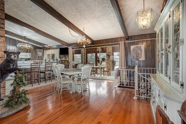 dining space featuring light wood-type flooring, a textured ceiling, vaulted ceiling with beams, and wooden walls