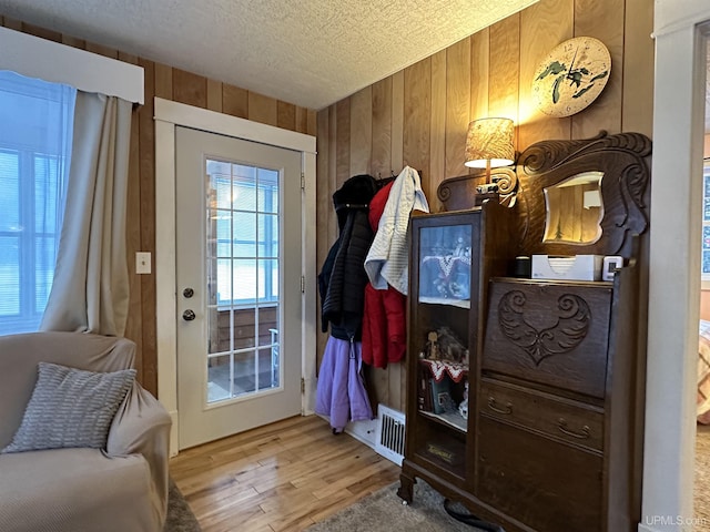 entryway featuring a textured ceiling, light hardwood / wood-style flooring, and wood walls