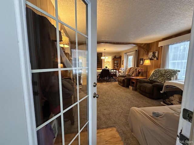 living room featuring carpet flooring, wood walls, a textured ceiling, and a chandelier