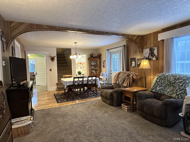 living room with light carpet, a textured ceiling, a notable chandelier, and wood walls