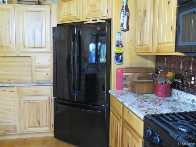 kitchen featuring light stone countertops, light brown cabinets, tasteful backsplash, and black appliances