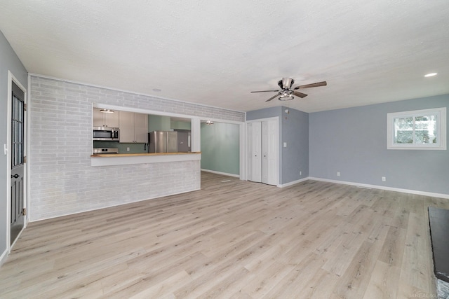 unfurnished living room featuring ceiling fan, a textured ceiling, brick wall, and light hardwood / wood-style flooring