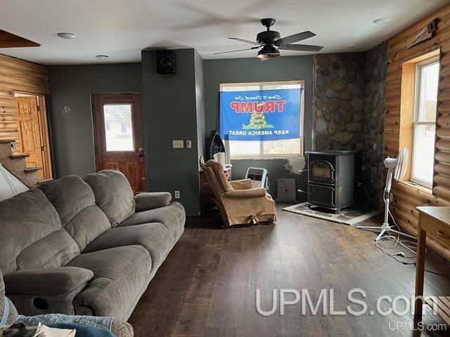 living room featuring a wood stove, rustic walls, ceiling fan, and wood-type flooring