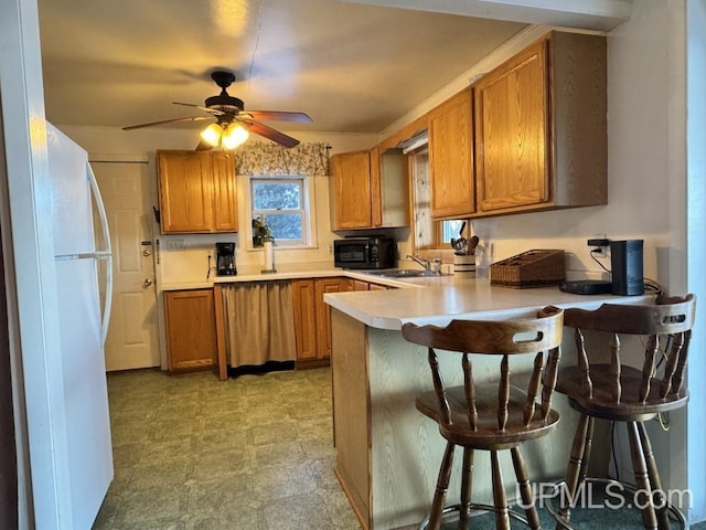 kitchen with a breakfast bar, white refrigerator, sink, ceiling fan, and kitchen peninsula